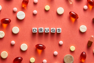 Black and white title DRUGS from white cubes on the table with tablets on coral background