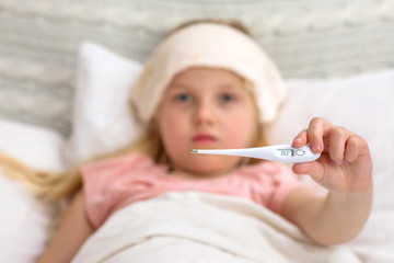 Sick little child girl lying in bed with thermometer. child shows a thermometer with high temperature