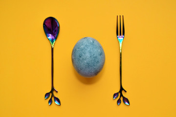 Blue egg with rainbow fork and spoon, painted in tea hibiscus, on yellow background, similar to marble with copyspace