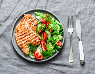 Grilled pork chops and tomatoes, cucumbers, greens salad on a gray background, top view. Healthy food diet concept