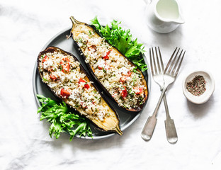 Baked eggplant stuffed with couscous, tomatoes, cilantro with yogurt sauce on a light background, top view