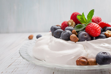 Pavlova cake with fresh summer berries and hazelnuts on glass plate.