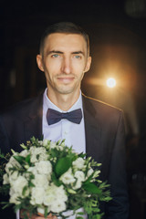 Portrait of Handsome Stylish groom holds white wedding bouquet.