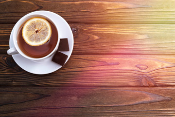 a Cup of tea with lemon, two pieces of chocolate on a wooden background.