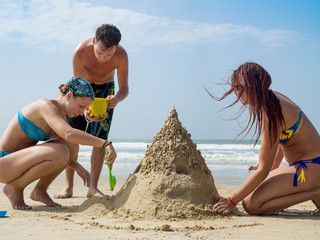A young company of people is building a sand castle on the beach