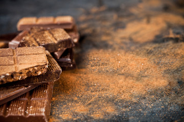 Broken chocolate  witn cinnamon powder stacked on black background.