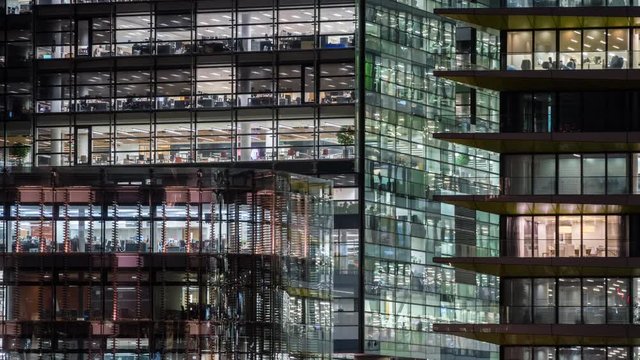 windows of the multi-storey building of glass and steel office lighting and working people within