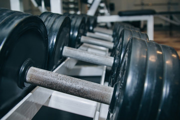 hand metal dumbbells lie together in a row on the rack in the gym close-up. training tools