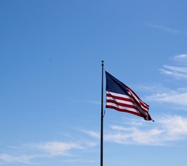 The united states flag flying in the wind with blue skies.