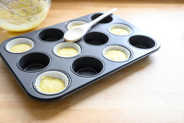 Obraz na płótnie Canvas muffin tin, half filled with paper cups and dough for cupcake baking on a wooden kitchen table, copy space