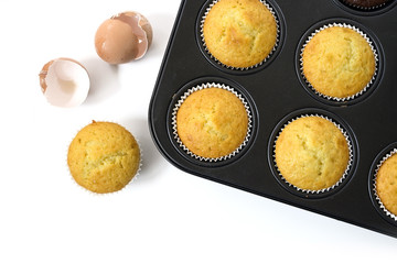 baked cupcake cakes in  a muffin tin and eggshells isolated with shadows on a white background,...