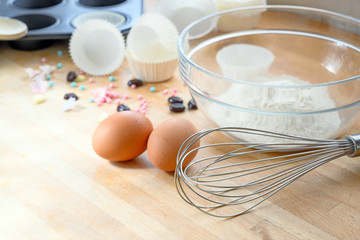 whisk, eggs, flour and muffin tin for cupcake baking on a wooden table, copy space