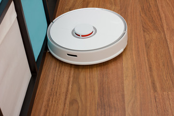 Automation cleaning. White robot vacuum cleaner collects dust, hair, washes the floor at home