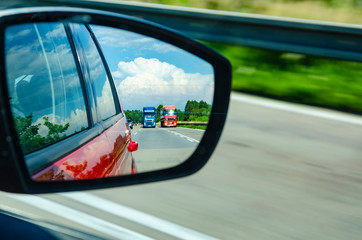 Reflection of two blurred overtaking trucks in the rearview mirror on highway