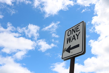 One way street sign against blue sky and clouds in urban neighborhood