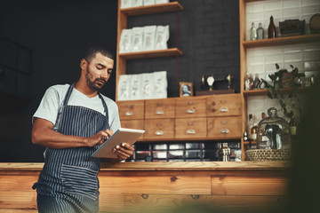Young man in apron using digital tablet at his cafe