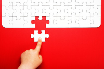 Children's hand moves a piece of white puzzle on a red background