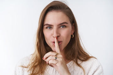 Fototapeta premium Flirty mysterious charming creative girlfriend asking friends stay quiet throwing surprise party showing shh shush gesture index finger pressed lips smiling, wants stay silent, white background