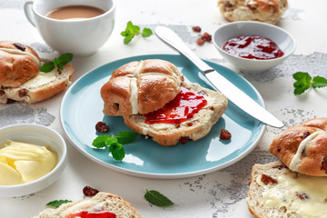 Hot cross buns in blue plate served with butter, strawberry jam and cup of tea