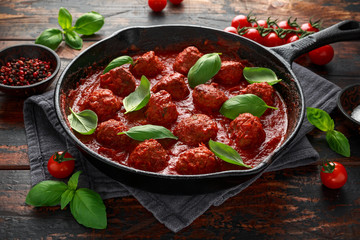 Homemade Meatballs in iron cast with sweet and hot tomato sauce, basil. On wooden table