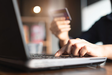 Woman's hands holding credit card and typing on the keyboard of laptop for shopping online. Pays for purchase.