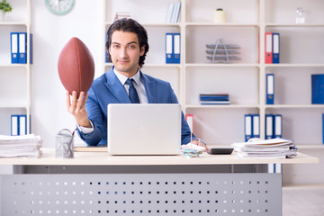 Young handsome businessman with rugby ball in the office