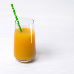 Tall glass of tasty freshly squeezed orange juice with green straw