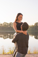 Romantic, people and summer concept - man raised a woman in his arms near the lake at the sunset