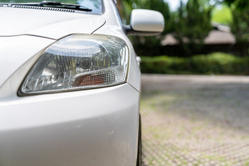 A part of front headlight of white car with blurred green park background