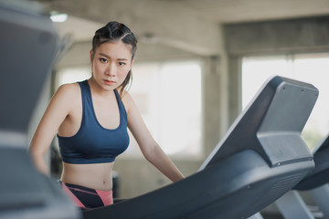 Fototapeta na wymiar Young asian woman walking and running on the running machine and looking at the camera at the gym. Woman workout at fitness room.