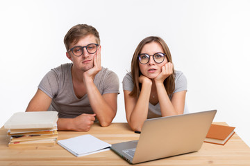 Education and people concept - couple of young people in glasses look like they are bored of learning homework