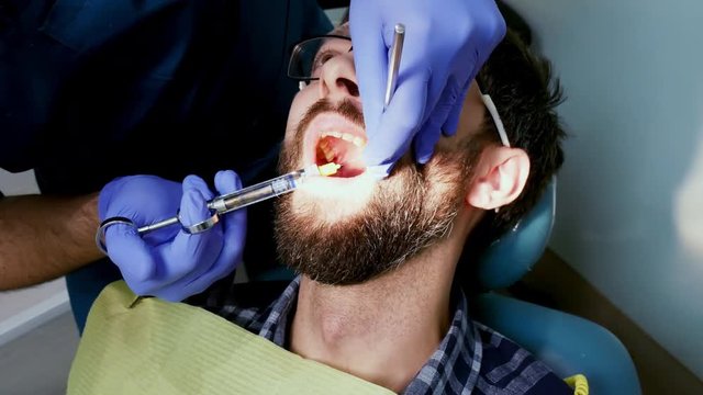 Anesthesia injection in patient tooth. Man with open mouth during dental procedure.