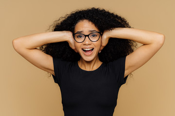 Young woman with curly Afro hair covers ears, shouts as demands be quiet, cant stand noise, keeps...