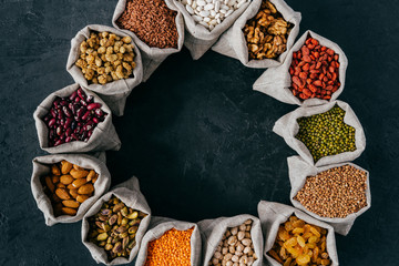 Top view of colorful nutritious cereals and dried fruit in small sacks standing in circle, isolated over dark background. Food concept