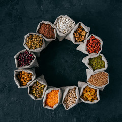 Photo of assorted legumes in hemp sacks standing around over dark background. Dried fruit, nuts and seeds. Agriculture concept