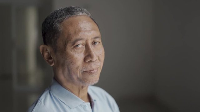 Elderly man recovering from stroke disease while sitting on wheelchair and smiling at the camera