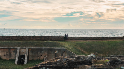 Senior couple traveller looking at the ocean when the sunset on a fort wall in Sri Lanka