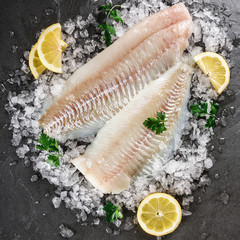 Fresh raw fillet white fish Pangasius with spices on ice over dark stone background.  Seafood, top...