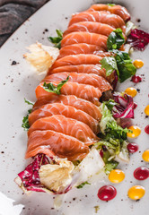 Salad of sliced salmon fillet with lettuce, cabbage and sauce in plate on dark grey background. Healthy food, clean eating, dieting, closeup