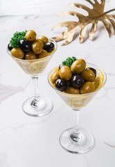 Black and green olives in glass on white marble background. Various kinds of Mediterranean pickled olives. Top view.