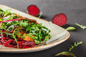 Healthy fresh salad with baked beets, greens, arugula, spinach and croutons in plate over dark table. Healthy vegan food, clean eating, dieting.