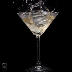 in a martini glass, vermouth ice falls, and splashes with drops on a black background