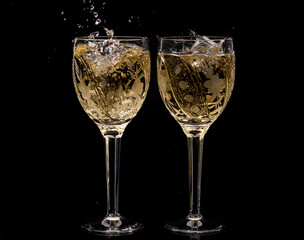 Two crystal wine glasses with a drink, falling ice and splashes