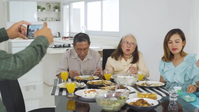 Happy three generation family taking photo in dining room at home. Shot in 4k resolution