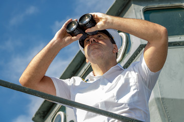 Captain of ship looking ahead. A sailor officer in white uniform looking to sea with binocular...