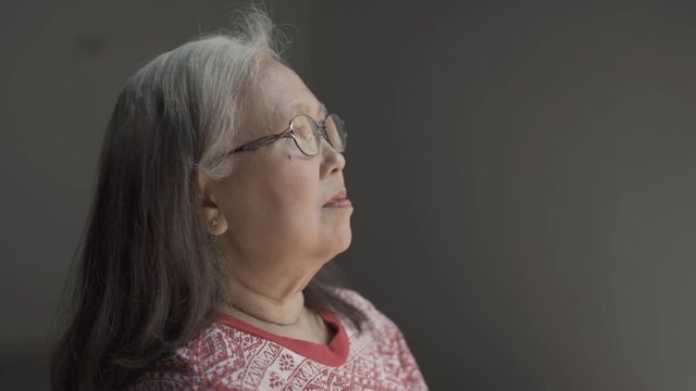Lonely senior woman sitting on wheelchair while looking on the window at home. Shot in 4k resolution