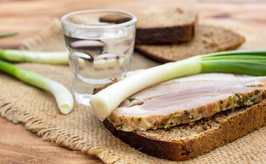 Glass of vodka with snack on the wooden table.