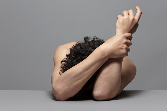 Homme en repli sur soi m&ecirc;me, studio fond gris