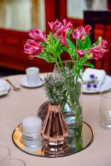 flower pots on the table, natural flowers, elegant table centerpiece with pink alstroemeria flowers, rose gold vase, and white candle on a mirrored tray, sophisticated event decor, vertical
