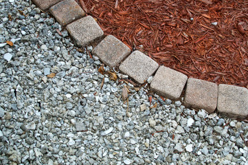 Looking down at square bricks form curve that separates mulch from gravel or small stones in...